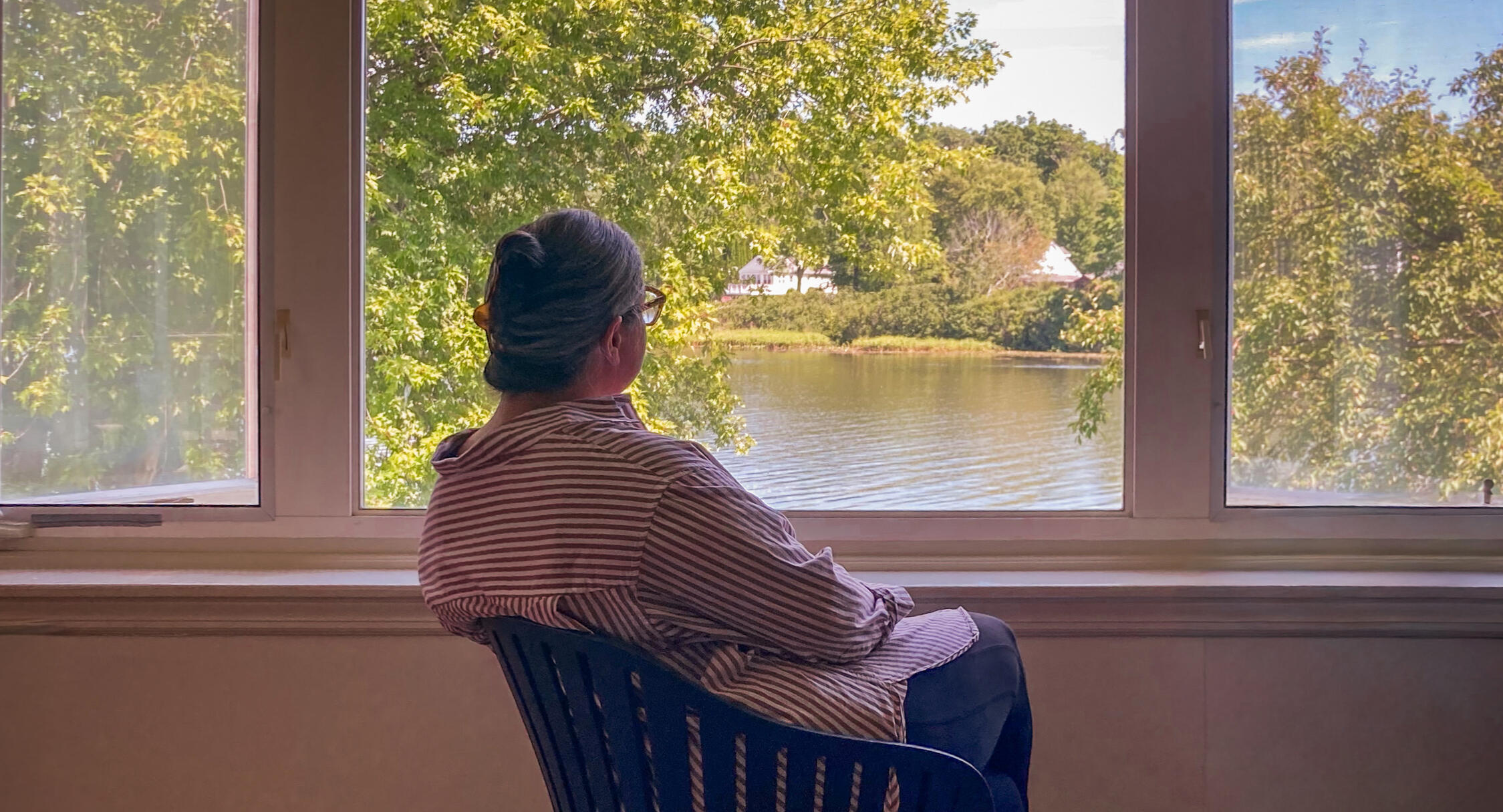 Woman Looking Out the Window Woman sitting in a chair, looking out the window over a lake.